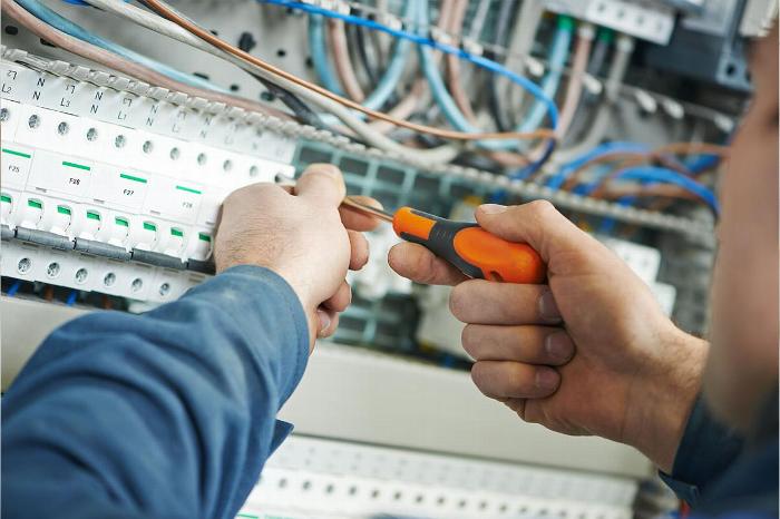 A technician using a screwdriver to work on electrical wiring inside a distribution panel.