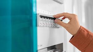 A close-up of a person's hand adjusting a circuit breaker switch on a panel in a brightly lit setting, showcasing an important aspect of electrical safety.