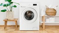 A modern washing machine in a bright, minimalistic laundry room setting with a potted plant, wooden stools, and decorative storage. Perfect for efficient cleaning and laundry tasks.