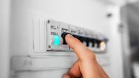 A hand pressing a switch on an electrical panel, with a blue light indicating power status, demonstrating electrical safety and control.